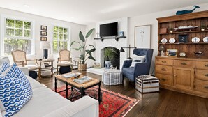 Una sala de estar con un sofá blanco, un sillón azul y un mueble de madera con objetos decorativos.