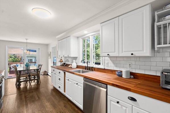A modern kitchen with white cabinetry, wooden countertops, and a built-in dishwasher. - Wellfleet Beach House (Wellfleet)