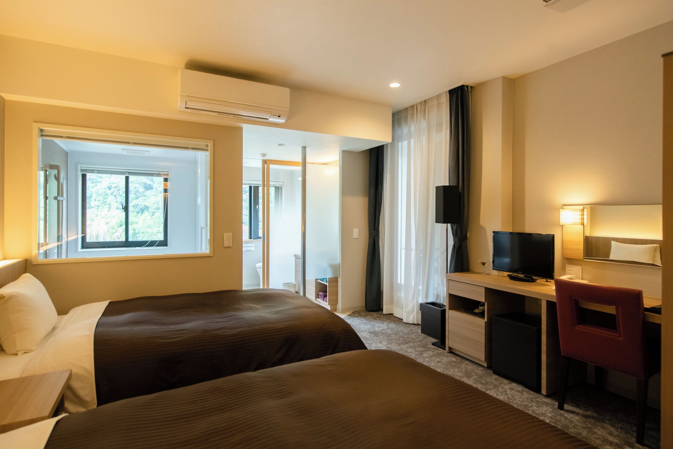 Una habitación de hotel con dos camas, un escritorio, un televisor y un aire acondicionado.