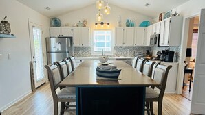 Una cocina moderna con armarios blancos, una mesa de comedor de madera y un televisor empotrado.