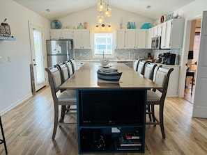 Una cocina moderna con armarios blancos, una mesa de comedor de madera y un televisor empotrado.