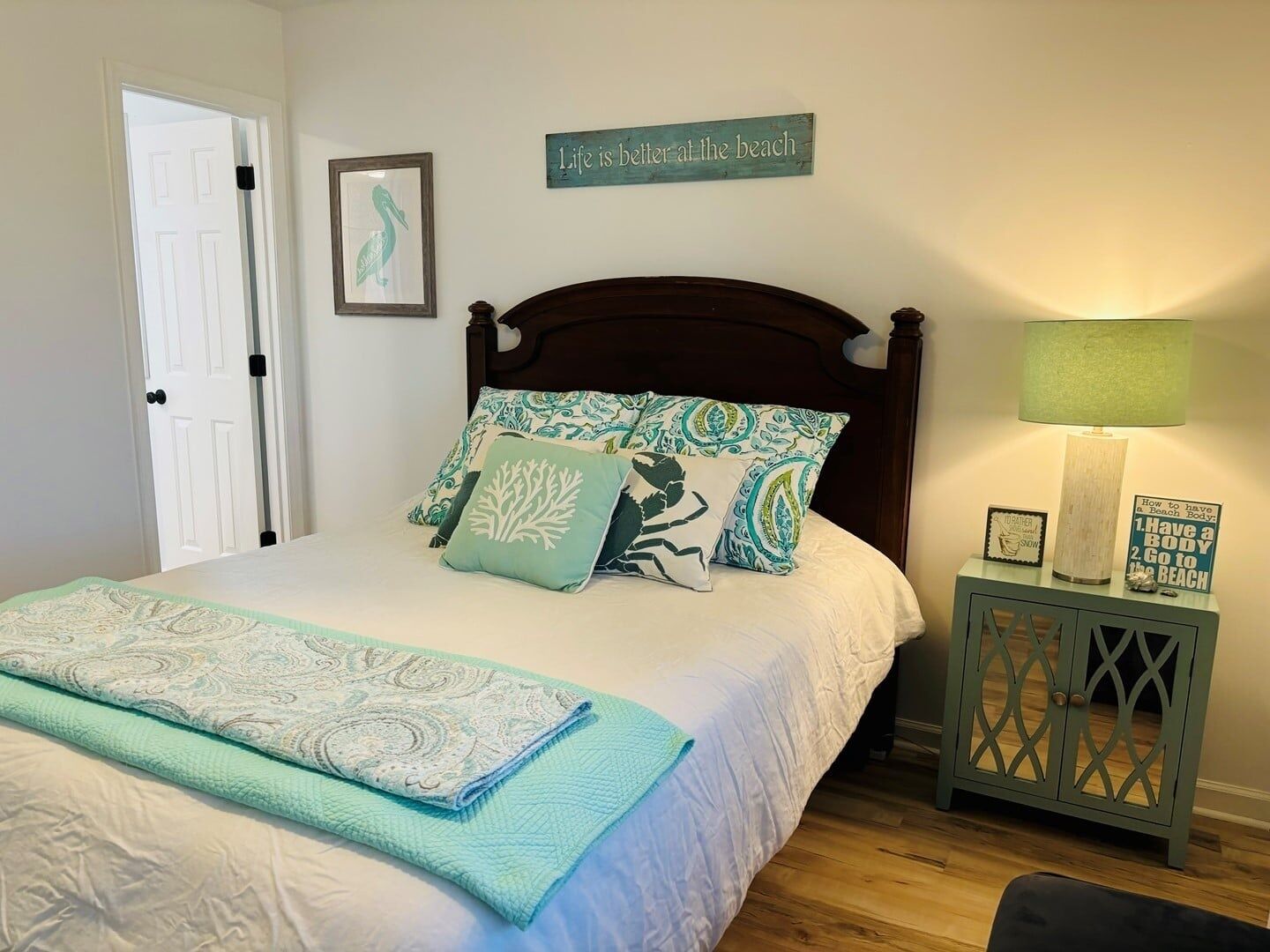 A bedroom with a bed, a bedside table with a lamp, a wall decoration, and a door.