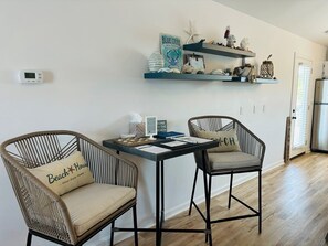 A kitchen with two wicker chairs, a table with papers, a thermostat, and a shelf with decorative items.