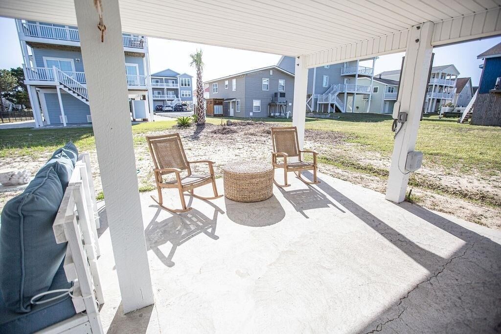 A covered outdoor seating area with wicker chairs and a round table, overlooking a residential neighborhood.