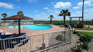 A pool area with lounge chairs, a small pavilion, and a view of the ocean. - Aquarius Condo Unit 207 2 Bedroom Condo by RedAwning (South Padre Island)
