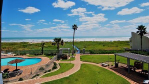 A pool area with a curved design, a pathway, and a view of the beach. - Aquarius Condo Unit 207 2 Bedroom Condo by RedAwning (South Padre Island)