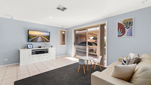 Un salon moderne doté d’un téléviseur à écran plat, d’un meuble de rangement blanc, d’un canapé gris et d’un coin repas avec une table et des chaises.
