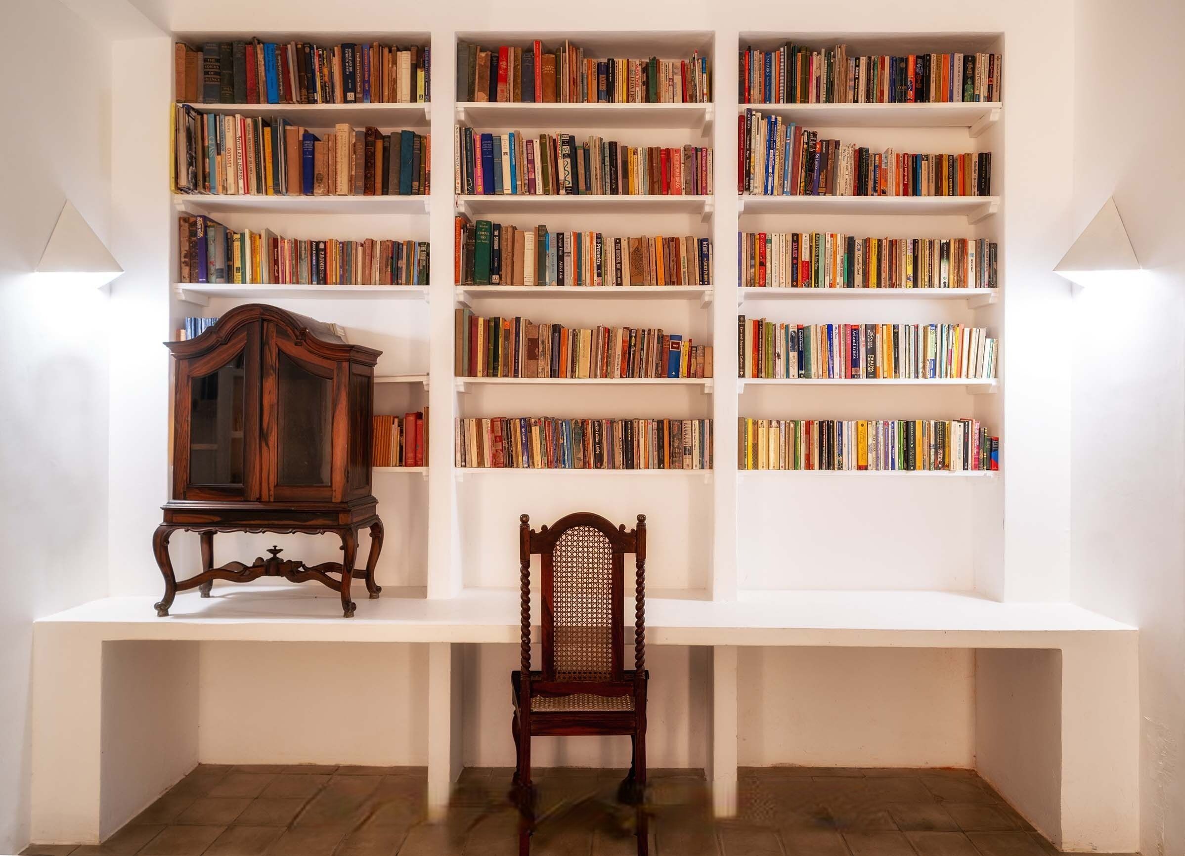 A room with a white bookshelf filled with books, a wooden chair, and a wooden cabinet.