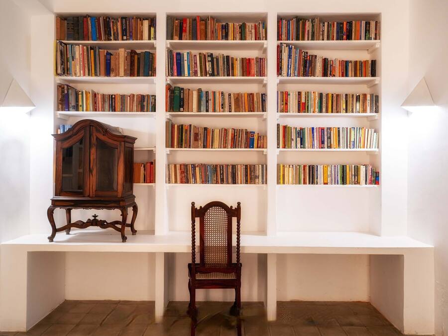 A room with a white bookshelf filled with books, a wooden chair, and a wooden cabinet.