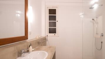 A bathroom with a white sink, a mirror, a shower, and a window.