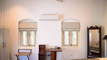 A bedroom with a bed, a desk, two windows with curtains, a wardrobe, and a ceiling fan.