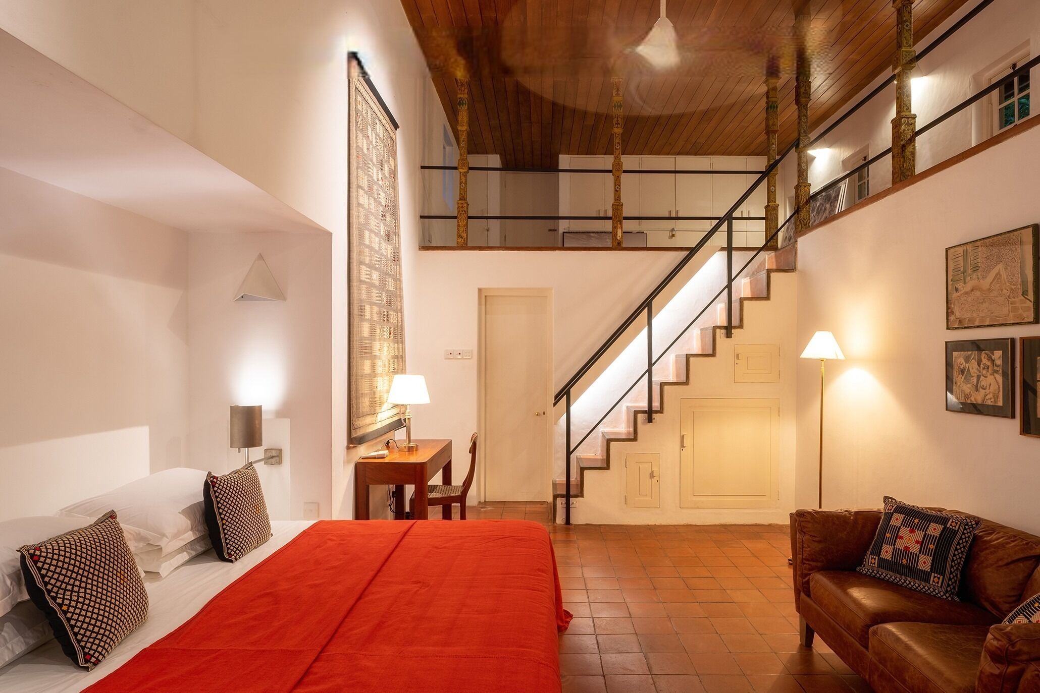 Une chambre d’hôtel comprenant un lit, un bureau, une chaise, un canapé, un escalier et une lampe fixée au mur.