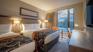 A hotel room with two beds, a desk, a chair, and a TV.