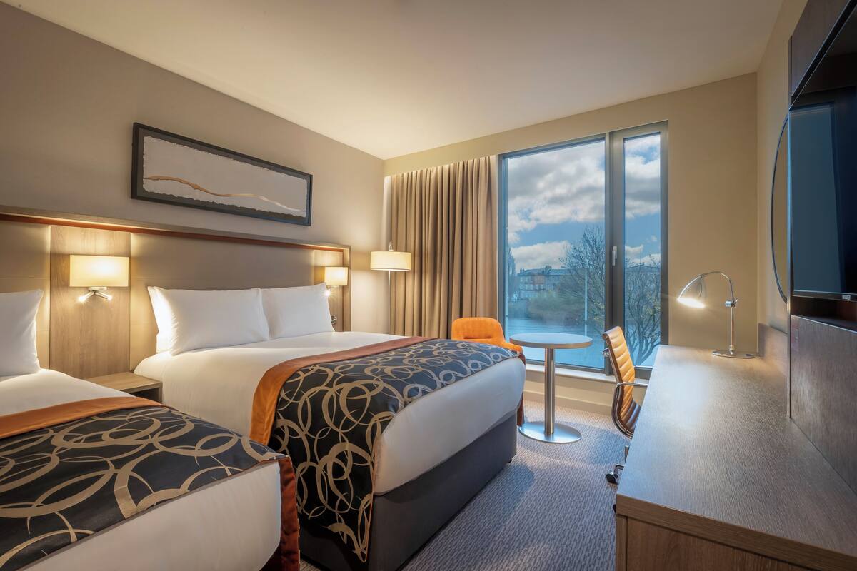 Une chambre d’hôtel avec deux lits, un bureau, une chaise et un téléviseur.