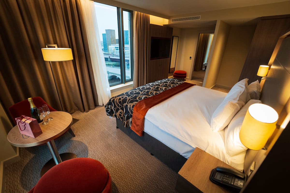 Une chambre d’hôtel équipée d’un lit, d’un bureau, d’une chaise, d’une télévision et d’une fenêtre donnant sur la ville.