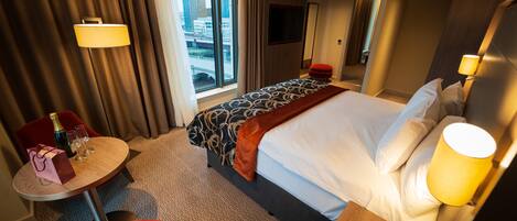 A hotel room with a bed, a desk, a chair, a TV, and a window with a city view.
