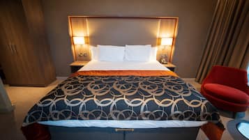 Ett hotellrum med en stor säng, två sänglampor, en röd stol och en garderob i trä.