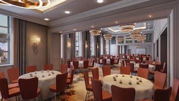 A conference room with multiple round tables and orange chairs, large windows, and modern lighting fixtures.