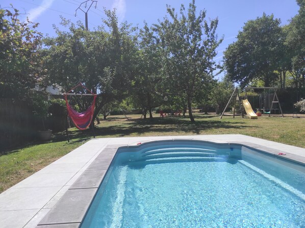 A swimming pool with a tiled deck, surrounded by trees and a hammock. - Quiet cottage with indoor pool in the Guérandaise countryside (Guérande)