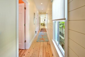 Un couloir doté d’un plancher en bois, d’un tapis orné de motifs d’étoiles de mer et d’une fenêtre donnant sur un paysage verdoyant.