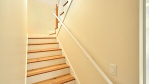 A staircase with wooden steps and white handrails, leading to a landing with a light switch. - Keys Breeze - Walk to Duval, Private Pool (Key West)