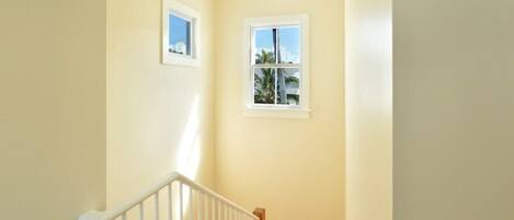 A staircase with white railings, wooden steps, and two small windows with white frames.
