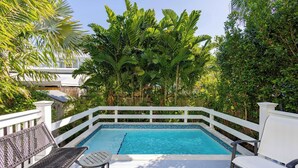 A swimming pool with a white deck, surrounded by lush greenery and a white fence. - Keys Breeze - Walk to Duval, Private Pool (Key West)