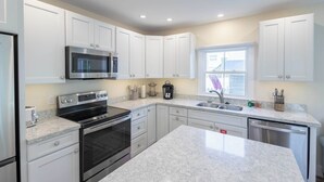 A modern kitchen with white cabinets, stainless steel appliances, a granite countertop, and a window providing natural light. - Keys Breeze - Walk to Duval, Private Pool (Key West)