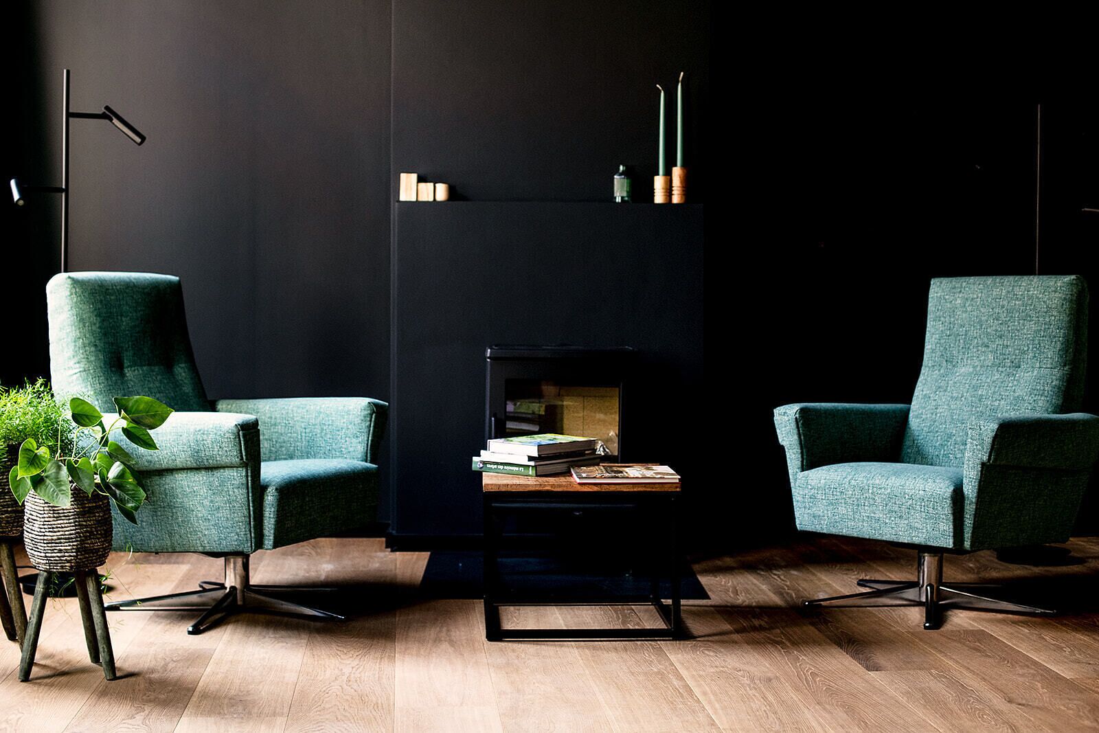 Een moderne woonkamer met twee smaragdgroene fauteuils, een zwarte salontafel en een open haard.