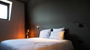 Een net opgemaakt bed met witte lakens in een moderne kamer met een donkere wand en een raam aan de linkerkant.