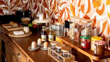 Una encimera de cocina con diversos alimentos y recipientes, incluyendo frascos de especias y una tabla de cortar de madera con pan.