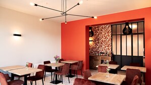 Een moderne eetruimte met houten tafels en rode bekleden stoelen, een decoratieve wand met een bladmotief, en een bijzondere hanglamp.