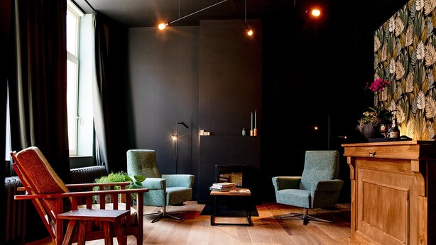 Een moderne zithoek met een donkere muur, houten vloer en drie groene fauteuils.