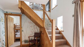 A wooden staircase with a cushioned landing, a chair, and a wall with floral wallpaper. - Anglers Barn (Skipton)
