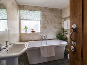 Une salle de bain avec une baignoire, un lavabo, une fenêtre avec une plante et un porte-serviettes.