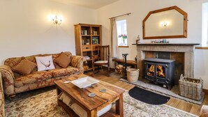 A cozy living room with a sofa, coffee table, fireplace, bookshelf, and a mirror. - Anglers Barn (Skipton)