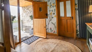 A room with a wooden door, a large window, a woven rug, and a wall with a floral mural. - Anglers Barn (Skipton)