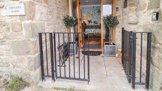 A stone building entrance with a wooden ceiling, a sign reading "Angler's Barn," and a metal gate. - Anglers Barn (Skipton)