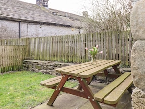 Une table de pique-nique en bois avec des bancs, située dans un espace aménagé en jardin.