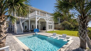 A swimming pool with a white deck, surrounded by palm trees and a house with a balcony. - Marsh front pool home with ocean, river and historical downtown views (St. Augustine)