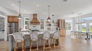 A spacious kitchen with a large island, wooden bar stools, and pendant lighting. - Marsh front pool home with ocean, river and historical downtown views (St. Augustine)