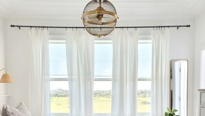 A bedroom with a large bed, a hanging light fixture, a view of the outdoors, and a dresser. - Marsh front pool home with ocean, river and historical downtown views (St. Augustine)