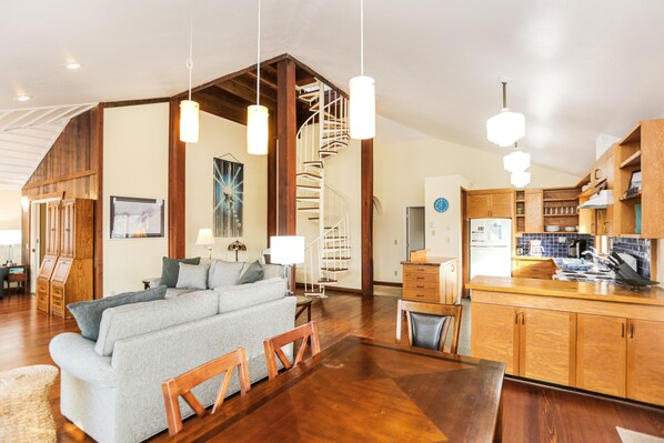 A spacious living area with a large sofa, wooden dining table, and a kitchen with wooden cabinets and a built-in stove.