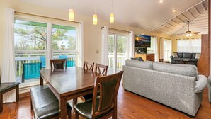 Un vaste espace de vie comprenant une table à manger, un canapé et un balcon offrant une vue sur les arbres.