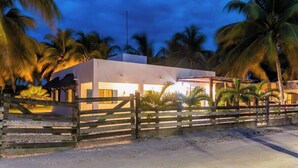 A modern building with a white facade, surrounded by a wooden fence and palm trees.