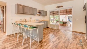 A modern kitchen with grey cabinets, a central island with bar stools, and a sliding glass door leading to an outdoor area.