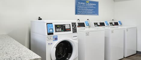 A laundry facility with four front-loading washing machines, a granite countertop, and a sign indicating it's for guests only.
