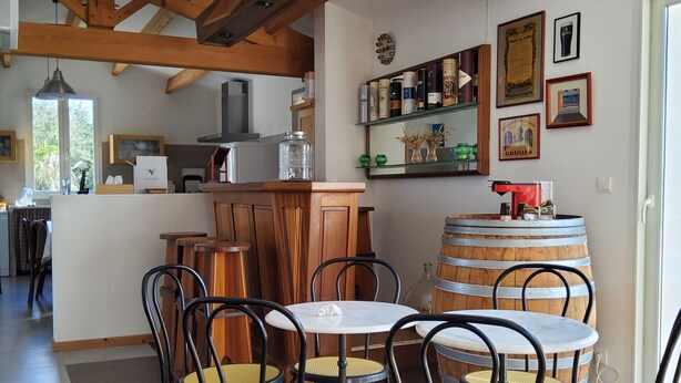 Un comedor con mesas y sillas de madera, una cocina al fondo y un barril grande.