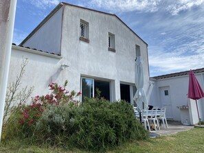 A white building with a large open door, a small window, and a patio area with chairs and an umbrella.