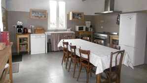 Una cocina con vigas de madera, una mesa de comedor con sillas, un refrigerador, un microondas, una estufa y una ventana con cortinas.
